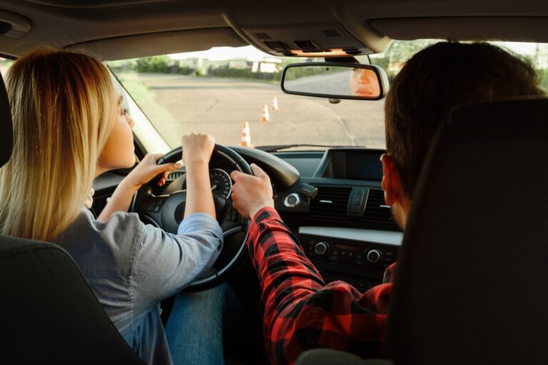 Driving instructor helping a woman steer during a driving lesson